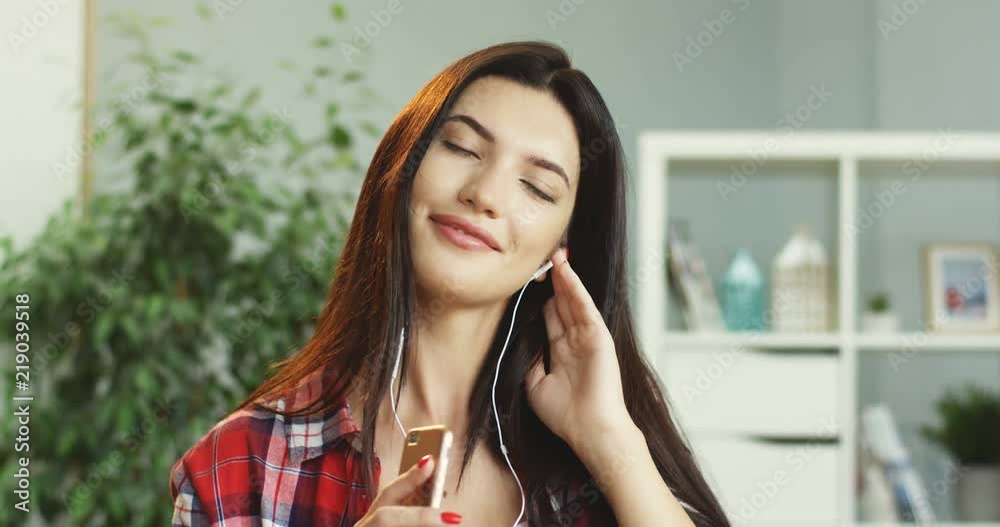 Portrait shot of the beautiful young brunette woman with eyes closed smiling and listening to the favourite music in the headphones on the smartphone. Portrait shot of the beautiful young brunette woman with eyes closed smiling and listening to the favourite music in the headphones on the smartphone.
