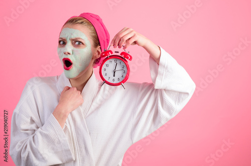 Cosmetic procedures. Surprised woman with cosmetic mask on face holds clock. Cosmetic mask. Natural ingredients. Wellness and Spa concept. Spa. Facial cosmetical mask. Time. photo