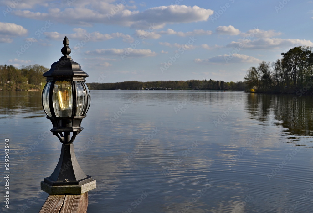 Lamp on a wooden railing over a water surface of a lake