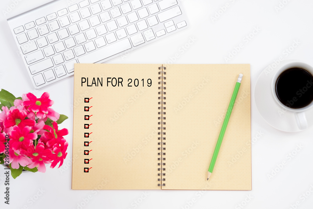 Note book with plan for 2019 word and check marks, keyboard, red flower, pencil and a cup of coffee on white table background. Note book with plan for 2019 word and check marks, keyboard, red flower, pencil and a cup of coffee on white table background.