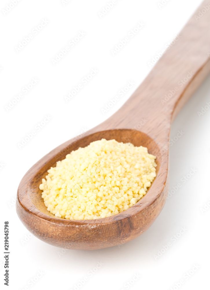 Heap of raw, uncooked couscous in wooden spoon over white