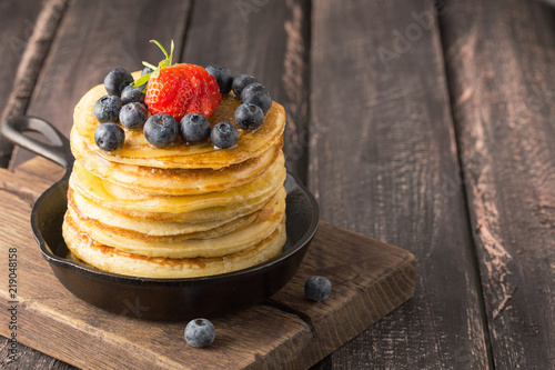 Buttermilk pancakes in cast iron pan served hot with maple syrup and fresh berries on rustic wooden table, healthy breakfast