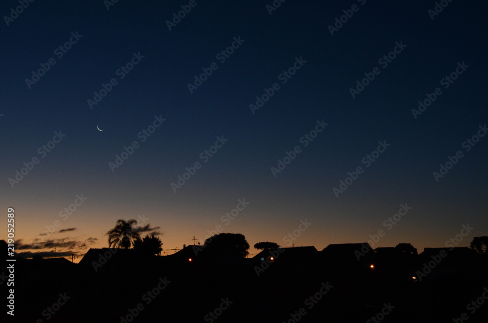 sunset with waning moon and silhouettes of houses sunset with waning moon and silhouettes of houses