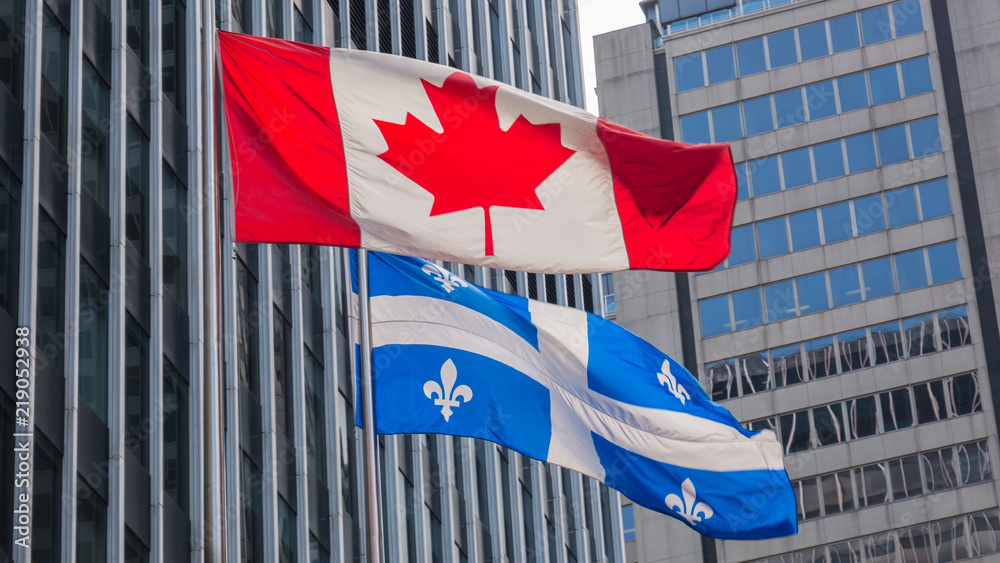 Fototapeta premium Quebec and Canada flags fluttering in the wind together in the downtown of Montreal.