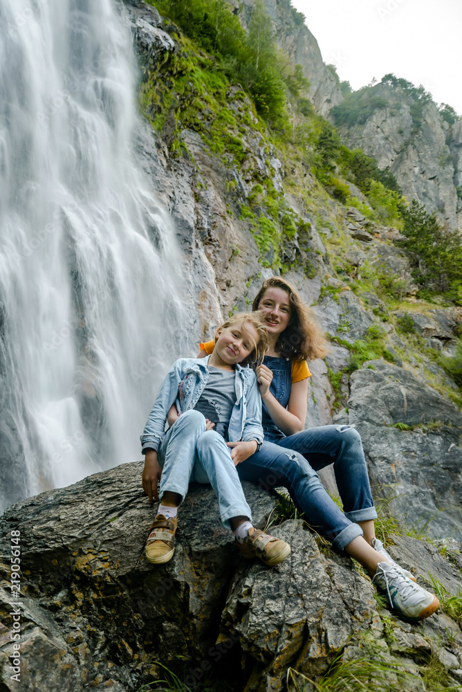 Naklejka premium Two sisters sitting on the stone on waterfall background