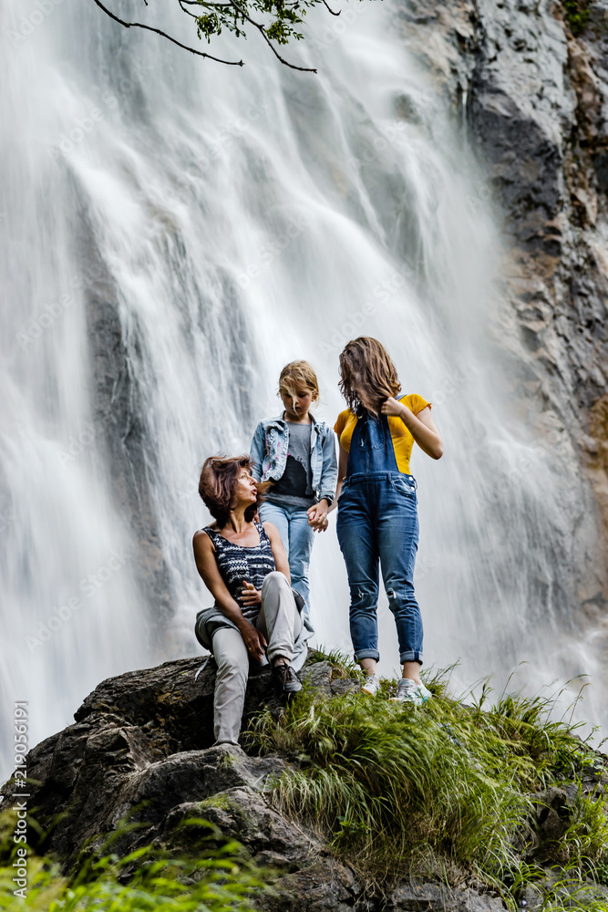 Two sisters with their mother sitting on the stone on waterfall background