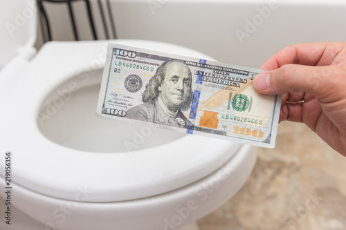 Holding crisp one hundred dollar bill into toilet; clena and bright; finance concept photo