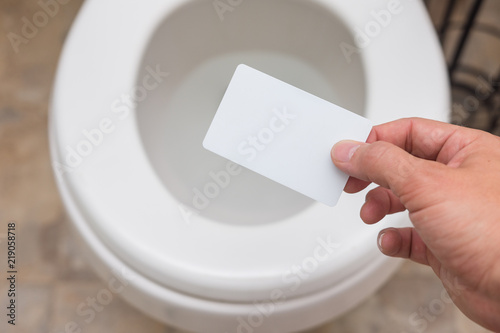 Holding blank card (credit card, membership card, coupon, drivers license) into toilet; bright and clean; finance concept