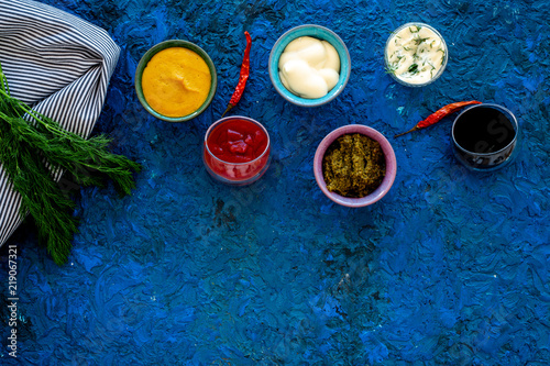Spicy sauses. Ketchup, mayonnaise, mustard, soy sauce, barbecue sauce, pesto, mustard, sour near chili pepper and greenery on blue background top view copy space © 9dreamstudio
