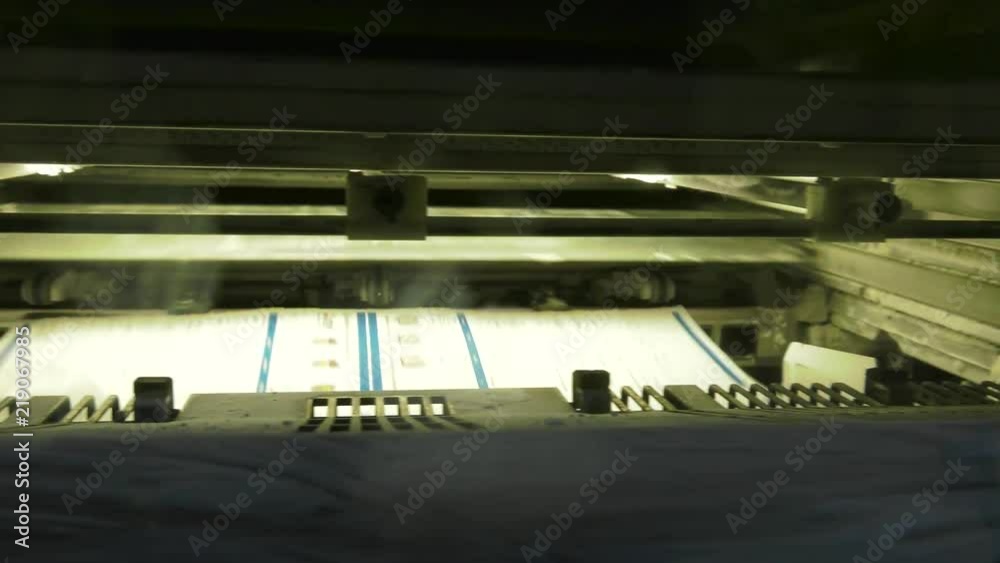 A large printing machine throws paper into a container. A large printing machine throws paper into a container.
