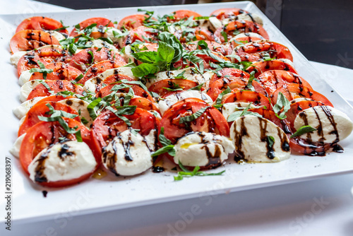 Tableau sur toile Caprese salad with mozzarella tomato, basil and balsamic vinegar arranged on whi