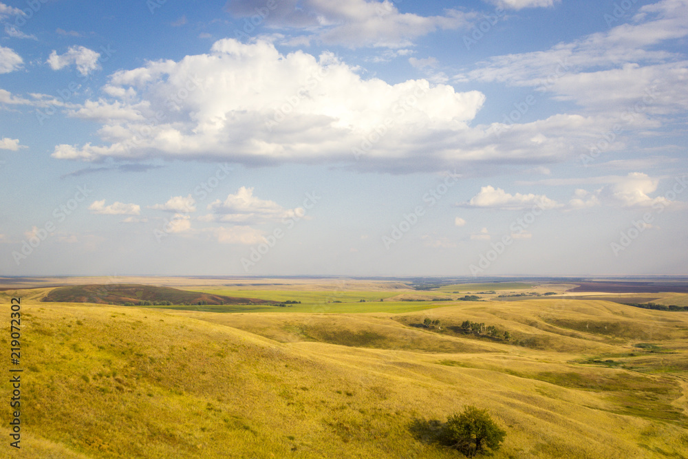 Summer landscape of fields and meadows with harvested crop, boundless expanses, blue sky with cumulus clouds, top view from mountain
