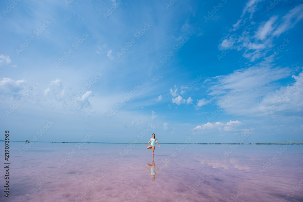 A beautiful woman in a mint body stands in a tree position in a pink salt lake. Redhead young woman doing yoga standing ankle-deep in water, pink salt lakes Bursol'