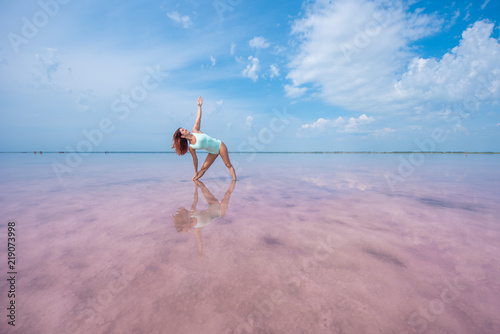 The girl on the shore of the pink lake is in the pose of a triangle. girl doing yoga on the ankle in the water of the pink lake. Trikonasana