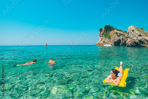 young pretty woman at yellow inflatable mattress. people swimming in clear water