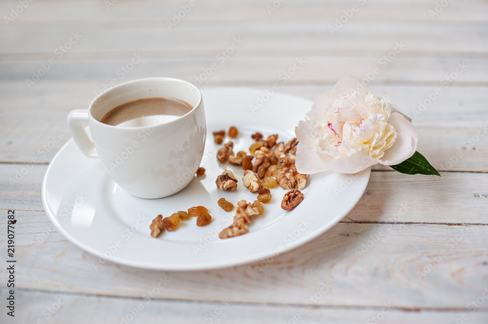 Cup of coffee with milk, nuts, sweets and a bud of a peony on a white saucer Cup of coffee with milk, nuts, sweets and a bud of a peony on a white saucer