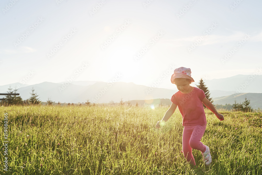 Cute happy little baby girl play outdoors in the lawn and admiring mountains view. Copy space for your text