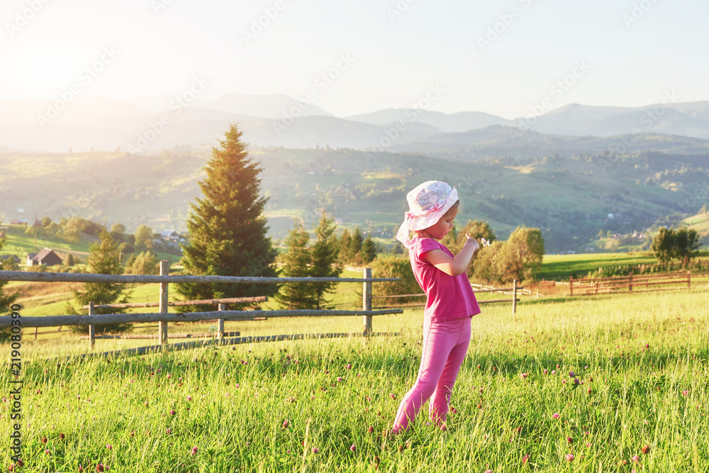 Cute happy little baby girl play outdoors in the lawn and admiring mountains view. Copy space for your text Cute happy little baby girl play outdoors in the lawn and admiring mountains view. Copy space for your text