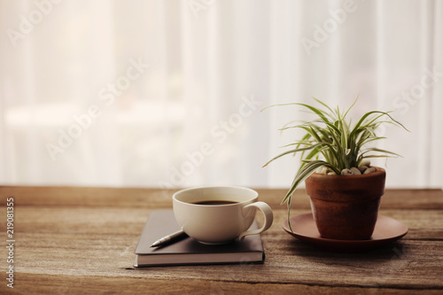 Coffee cup and black notebook with pen and plants on wooden table