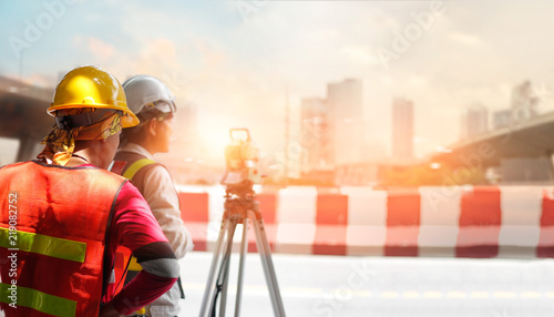 Surveyor builder and engineer working with theodolite transit equipment at construction site outdoors on street in sunlight in the city background photo