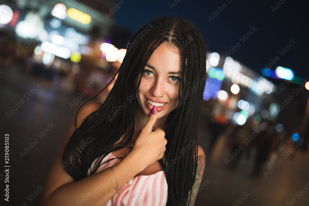 Sexy attractive woman holding finger on lips in night city street