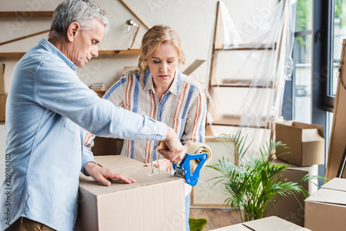 focused senior couple packing cardboard boxes while moving home © LIGHTFIELD STUDIOS
