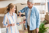 happy senior man pouring wine to wife while celebrating relocation
