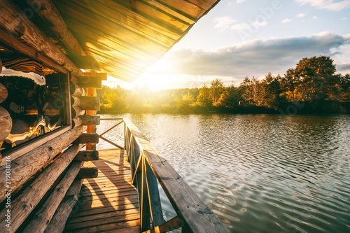 Fototapeta Naklejka Na Ścianę i Meble -  Wooden house with a terrace on the water at the lake, at sunset, a beautiful river bank at sunset