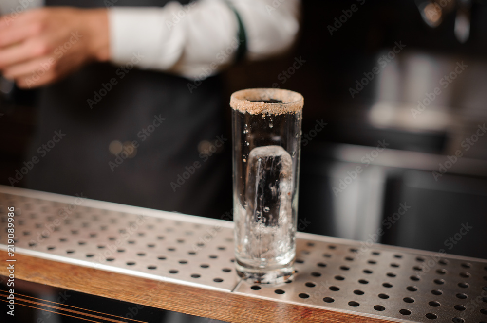Cocktail glass with an ice cube and sugar edge on the bar counter