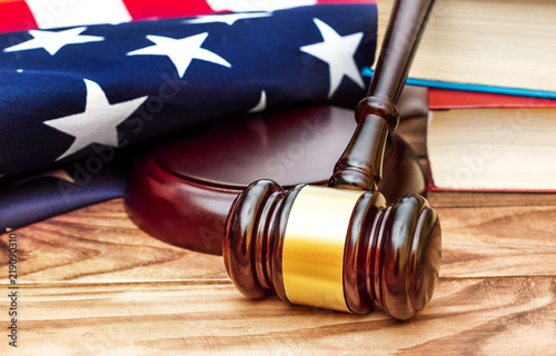 Judge's gavel with stack of books and american flag on the table.