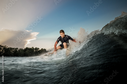 Young active man riding on the wakeboard on the bending knees
