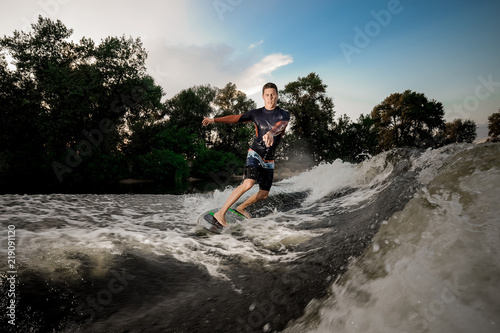 Young attractive man riding on the wakeboard on the lake