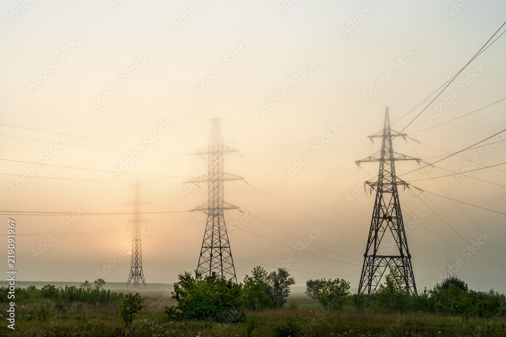 High voltage transmission towers in meadow at orange sunset 

