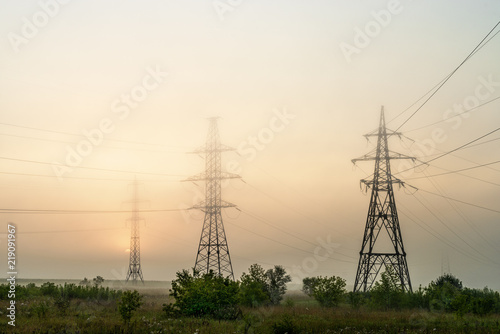 High voltage transmission towers in meadow at orange sunset 
