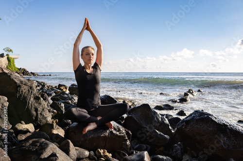 Young woman in black doing her yoga on asian rock beach © rostovtsevayu