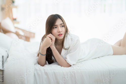 A beautiful young woman lying in bed comfortably and happily. Happy morning. Portrait of a smiling pretty girl relaxing in white bed.