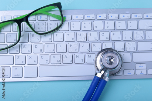 Closeup of a blue stethoscope lying on notebook keyboard and green glasses. selective focus. photo