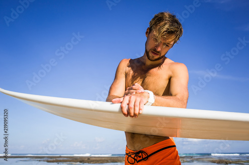 Photography athletic sportsman with surfing board checking time on coastline on summer day