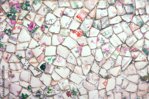 Mosaic made of broken crockery and tableware background. Wall tiled with ceramic pieces having floral pattern and Chinese hieroglyphs meaning: rich, blessing, tea, four