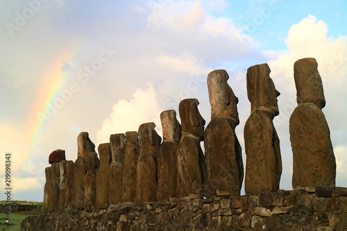 Amazing view of the back of 15 huge Moai statues of Ahu Tongariki with the rainbow on cloudy sky in background, Easter Island, Chile