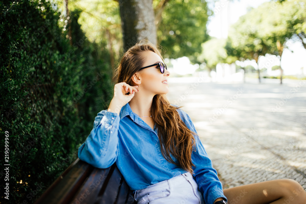 Happy Beautiful young woman sits on a bench in a summer park Happy Beautiful young woman sits on a bench in a summer park