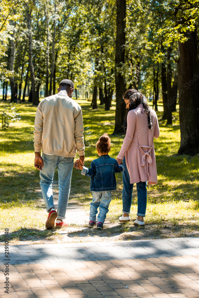 back view of african american parents and daughter walking in park on weekend back view of african american parents and daughter walking in park on weekend