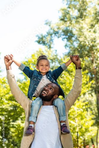 Slika na platnu happy african american father holding daughter on shoulders in park