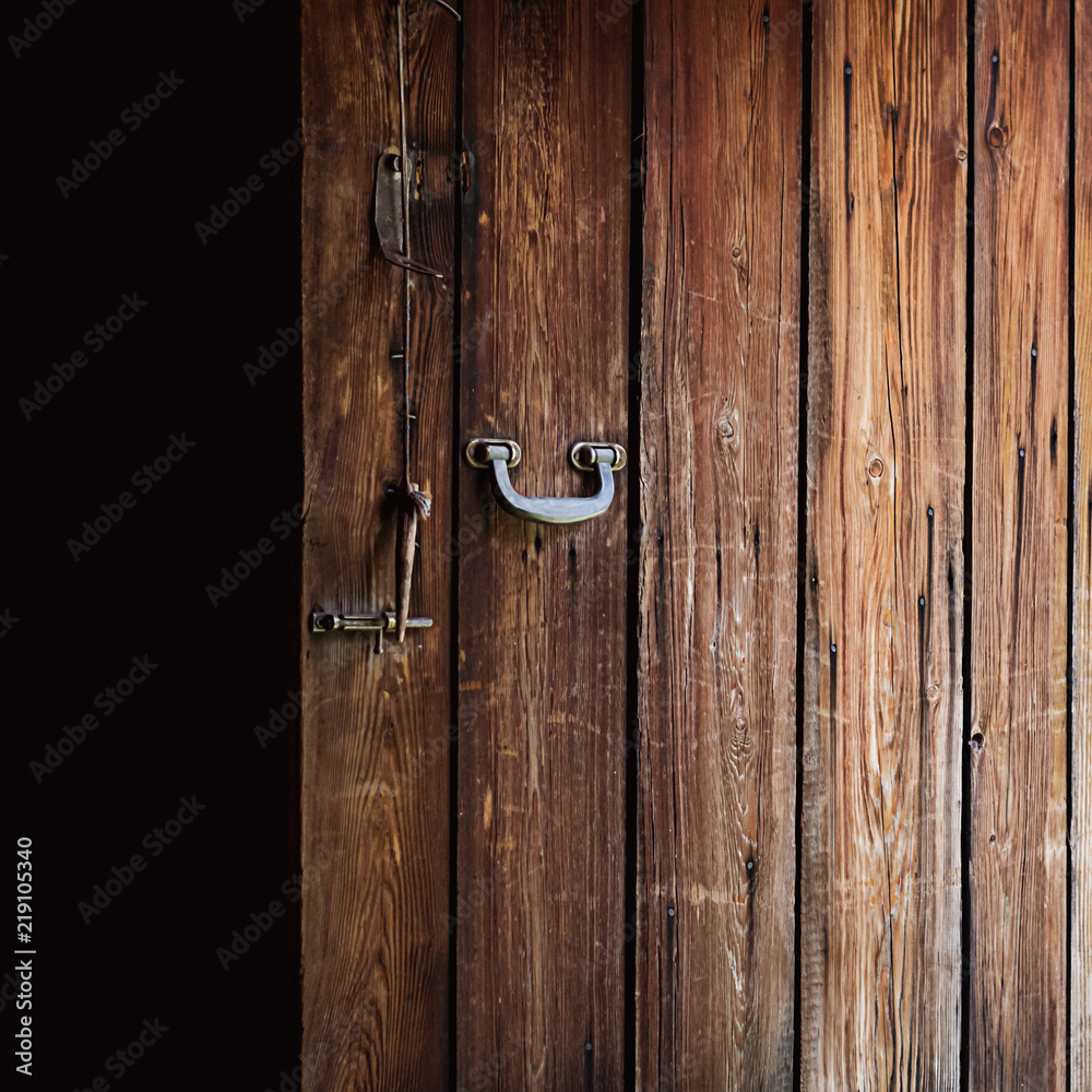 Opened old weathered wooden door with polished metal handle, steel latch and wooden bolt hanging on a string Opened old weathered wooden door with polished metal handle, steel latch and wooden bolt hanging on a string