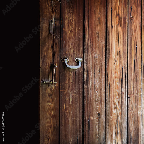 Opened old weathered wooden door with polished metal handle, steel latch and wooden bolt hanging on a string