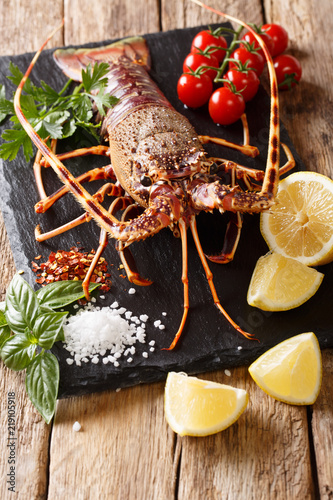 Raw spiny lobster with spices, vegetables ingredients close-up on a black board on a table. Vertical