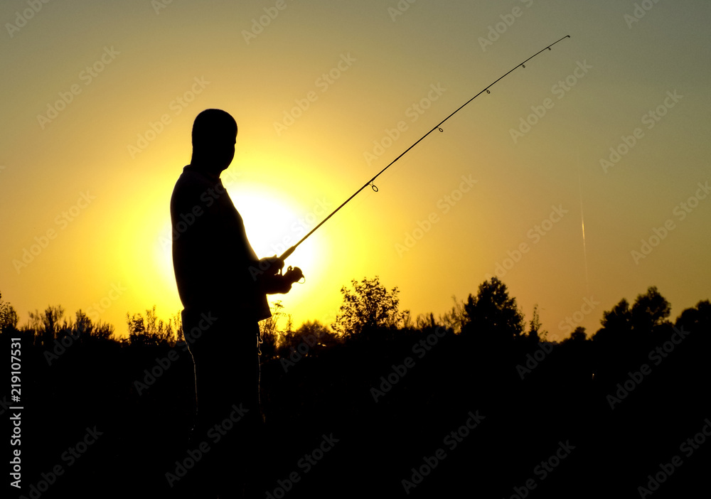 silhouette of fisherman with fishing rod on sunset background