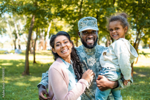Happy African American soldier in military uniform looking at camera with family in park photo