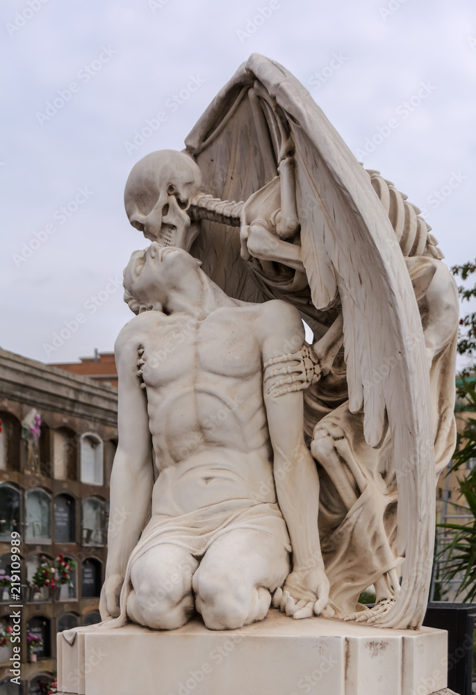 The Kiss of Death statue in Poblenou Cemetery in Barcelona. This marble sculpture depicts death, as a winged skeleton, kissing a handsome young man. The sculpture is at once romantic and horrifying.
