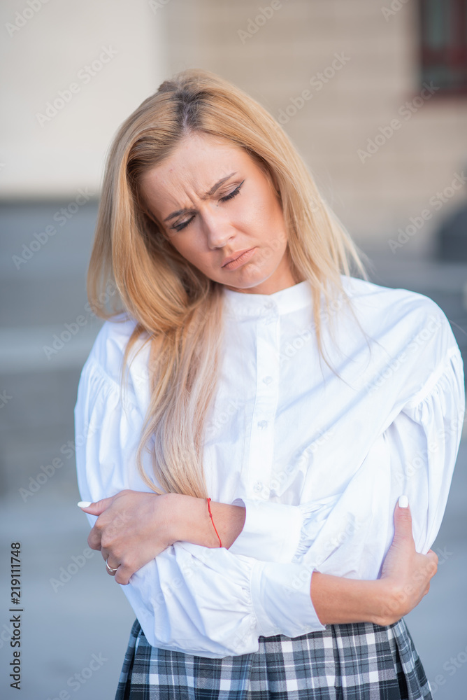 pensive young blond woman on building background with columns. sad girl in a white blouse